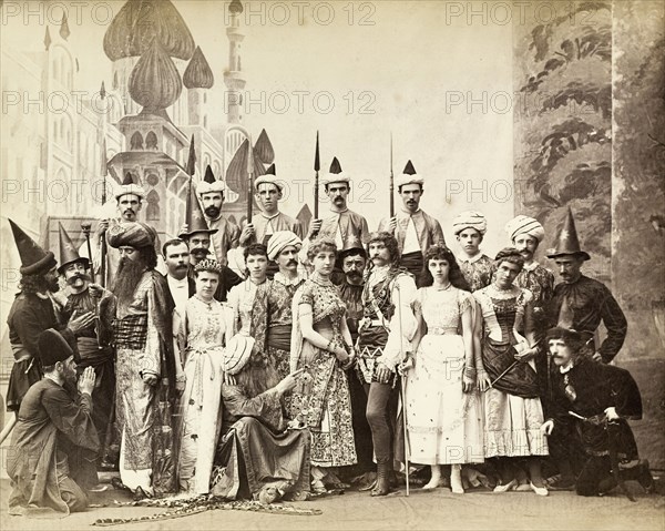 Cast of Lalla Rookh. The European cast in a pantomime of Lalla Rookh. The group stand on stage in front of a painted backcloth, dressed in Oriental and medieval costumes with accessories including turbans, sorcerer's pointed hats, cummerbunds, scimitars and exaggerated beards. Calcutta (Kolkata), India, circa 1885. Kolkata, West Bengal, India, Southern Asia, Asia.