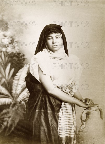 Egyptian woman. Studio portrait of a young Egyptian woman, posed in traditional dress, her hands resting on an ornamental urn. Probably Egypt, circa 1885. Egypt, Northern Africa, Africa.