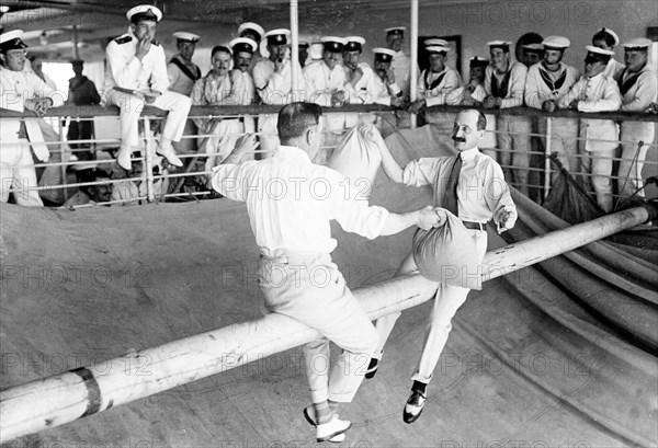 Pillow fight aboard HMS Medina. Major Lord Charles Fitzmaurice (left), Equerry to King George V, and Lord Shaftesbury, the Lord Chamberlain, stage a pillow fight on a greased spar aboard HMS Medina. The royal yacht was transporting King George V and Queen Mary to India for the Coronation Durbar at Delhi. Indian Ocean near Mumbai, India, circa 30 November 1911. India, Southern Asia, Asia.
