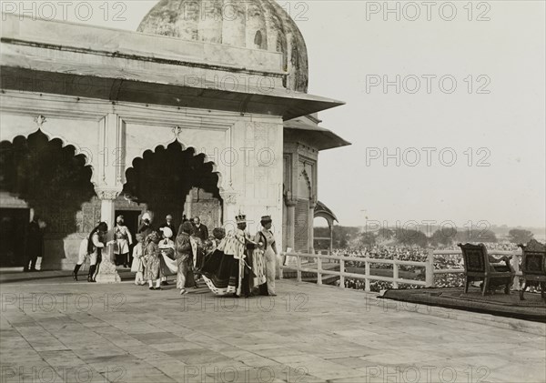 The royal couple at the Delhi Fort. King George V (r.1910-36) and Queen Mary emerge before crowds onto a throned balcony at the Delhi Fort. Pictured the day after the Coronation Durbar, they are dressed in their coronation robes and crowns, and are accompanied by ten Indian pages. New Delhi, India, 13 December 1911. India, Southern Asia, Asia.