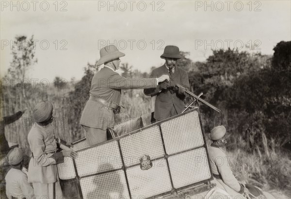 Assisting King George V. A royal aide assists King George V (r.1910-36) to load his rifle during a hunt in Chitwan Valley hosted by the Maharajah of Nepal. The pair are pictured standing in a howdah on the back of an elephant. Narayani, Nepal, 18 December 1911., Narayani, Nepal, Southern Asia, Asia.