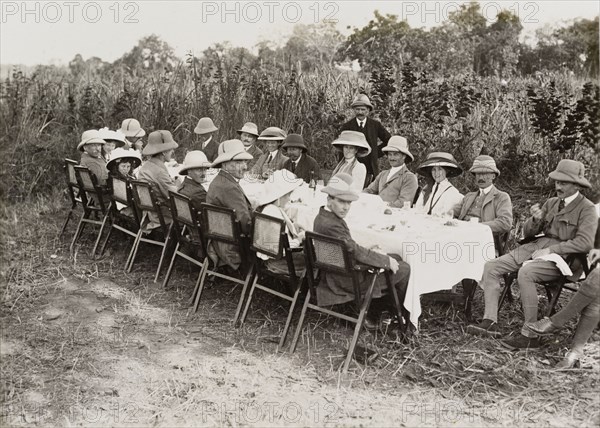 Royal lunch in the jungle. King George V (r.1910-36), seated fourth from left on the far side of the table, takes lunch in the jungle with his hunting companions. The King travelled to Nepal to hunt in Chitwan Valley following his Coronation Durbar in Delhi. Narayani, Nepal, 18 December 1911., Narayani, Nepal, Southern Asia, Asia.
