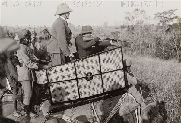 King George V takes aim. King George V (r.1910-36) aims his rifle at a tiger during a hunt hosted by the Maharajah of Nepal in Chitwan Valley. He crouches low in a howdah on the back of an elephant, accompanied by a royal aide. Narayani, Nepal, 18 December 1911., Narayani, Nepal, Southern Asia, Asia.