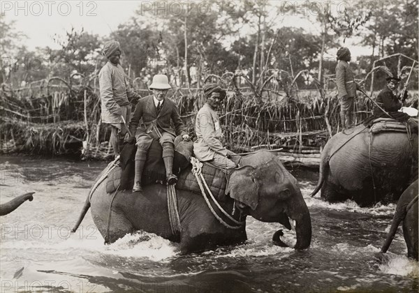 Sir Henry keeps his feet dry. Sir Edward Henry, Commissioner of the Metropolitan Police in London, rides sidesaddle on an elephant as he crosses a river during a royal hunt in Chitwan Valley. The Maharajah of Nepal hosted the hunt for King George V shortly after the Coronation Durbar in Delhi. Narayani, Nepal, circa 18 December 1911., Narayani, Nepal, Southern Asia, Asia.
