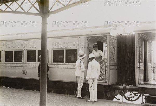 Queen Mary leans from the royal train. Queen Mary leans from the royal train to talk with Sir Derek Keppel and Sir Charles Cust. The train stands at an Indian railway station en route from Kolkata to Mumbai. India, circa 4 January 1912. India, Southern Asia, Asia.