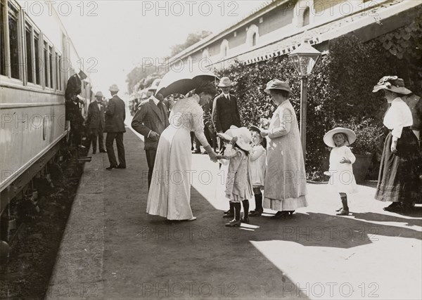 Queen Mary greets children. Shaded by her parasol, Queen Mary greets European children on a railway platform, en route from Kolkata to Mumbai. India, circa 4 January 1912. India, Southern Asia, Asia.