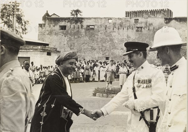 Officials at a Mombassan 'baraza'. The Liwali (Muslim government representative) of Mombasa, Sheikh Al'Amin bin Said El-Mandhry, shakes hands with E.G. Wright, the Senior Superintendent of Police in Mombasa. The pair were attending a 'baraza' (assembly) held to mark the Islamic pilgrimage of Hajj. Mombasa, Kenya, 15 May 1962. Mombasa, Coast, Kenya, Eastern Africa, Africa.