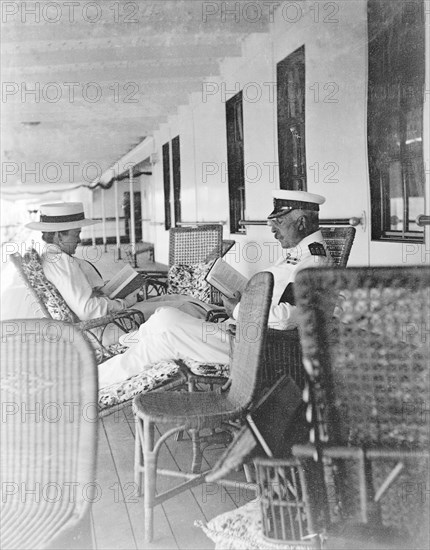 Duke and Duchess of Connaught on deck. The Duke and Duchess of Connaught sit in lounge chairs, reading books on the deck of the S.S. Balmoral Castle. The royal couple were travelling to South Africa to open the new Union Parliament in Cape Town. Probably Atlantic Ocean, Africa, October 1910. Africa.