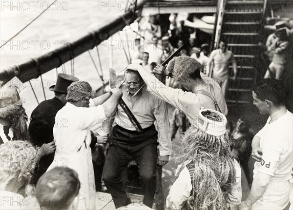 Antics aboard the S.S. Balmoral Castle. Crew members aboard the S.S. Balmoral Castle clown about on deck wearing costumes and wigs, possibly for a traditional 'crossing the line' naval initiation ceremony. The ship was transporting the Duke and Duchess of Connaught to South Africa, where they were due to open the new Union Parliament in Cape Town. Probably Atlantic Ocean, Africa, October 1910. Africa.