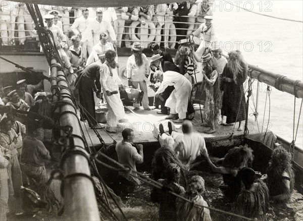 Antics aboard the S.S. Balmoral Castle. Crew members aboard the S.S. Balmoral Castle clown about on deck wearing costumes and wigs, possibly for a traditional 'crossing the line' naval initiation ceremony. The ship was transporting the Duke and Duchess of Connaught to South Africa, where they were due to open the new Union Parliament in Cape Town. Probably Atlantic Ocean, Africa, October 1910. Africa.