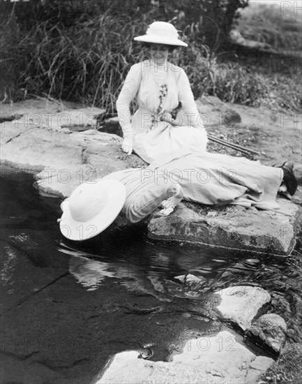 Duchess of Connaught at Victoria Falls. The Duchess of Connaught smiles as her female companion, probably her daughter Princess Patricia, leans over the edge of a shallow river on a day trip to Victoria Falls. This was one of several stops made by the Duke and his royal entourage following an official visit to Cape Town to open the new Union Parliament. Matabeleland, Southern Rhodesia (Matabeleland North, Zimbabwe), 12 November 1910., Matabeleland North, Zimbabwe, Southern Africa, Africa.