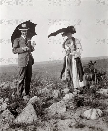 The Duchess of Connaught on tour. The Duchess of Connaught and a member of her royal entourage shelter from the sun beneath parasols on a rocky plain near Livingstone. This was one of several stops made by the Duke and Duchess following their official visit to Cape Town to open the new Union Parliament. Near Livingstone, Northern Rhodesia (Zambia), 12-15 November 1910., South (Zambia), Zambia, Southern Africa, Africa.