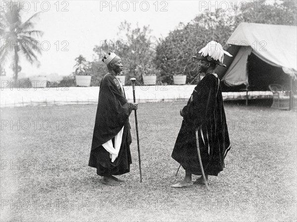 Two Bechuanaland chiefs. Two finely dressed Bechuanaland chiefs stand facing each other at an outdoor reception held for the Duke and Duchess of Connaught. One wears a crown and carries a staff: the other, a feathered hat and curved sword. Gaberones, Bechuanaland (Gaborone, Botswana), 24 November 1910. Gaborone, South East (Botswana), Botswana, Southern Africa, Africa.