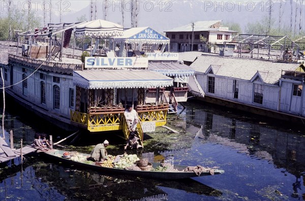 River tradesman on Dhal Lake. A river tradesman travels between houseboats moored on Dhal Lake, selling fruit and vegetables from his canoe. Sringarar, India, circa May 1976. Srinagar, Jammu and Kashmir, India, Southern Asia, Asia.