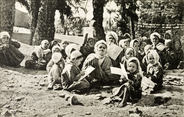 Outdoors school, Egypt. A group of young children sit cross-legged on a patch of desert sand as they take their lessons at an outdoors school. Egypt, circa 1925. Egypt, Northern Africa, Africa.