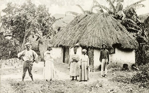 A Jamaican family. A Jamaican family pose for the camera outside a thatched roof dwelling. Jamaica, circa 1905. Jamaica, Caribbean, North America .