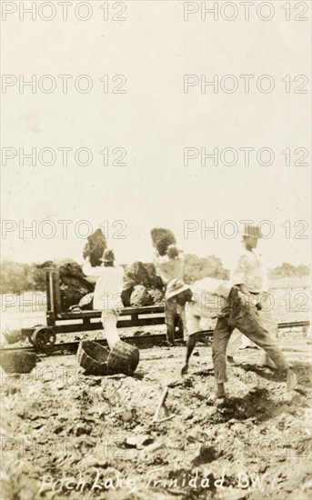 Extracting asphalt from the Pitch Lake. Labourers load lumps of asphalt extracted from Trinidad's Pitch Lake onto a waiting rail car. La Brea, Trinidad, circa 1910. La Brea, Trinidad and Tobago, Trinidad and Tobago, Caribbean, North America .