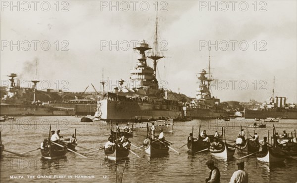 The Grand Fleet at Malta. Several small luzzus (row boats) share a Maltese harbour with two huge cruisers belonging to the Royal Navy's Grand Fleet. Malta, circa 1930., Malta, Malta, Central Europe, Europe .