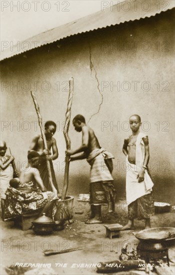 Pounding fufu. Two women prepare fufu, a staple food of West and Central Africa, by pounding the starchy mixture using a large pestle and mortar. Gold Coast (Ghana), circa 1910. Ghana, Western Africa, Africa.