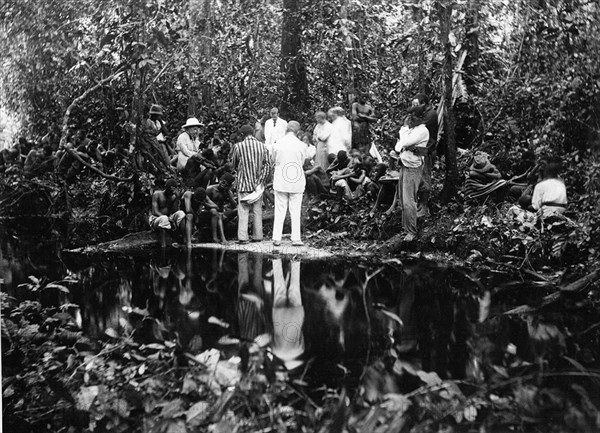 Forest prayer meeting. European and Congolese Christians are absorbed in prayer at a meeting on the banks of a forest stream. Alice Seeley Harris, a European missionary, appears on the left wearing a solatopi hat. Congo Free State (Democratic Republic of Congo), circa 1905. Congo, Democratic Republic of, Central Africa, Africa.