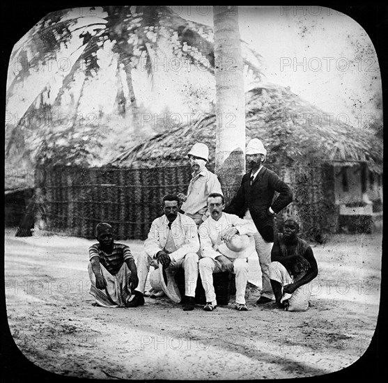 Consuls and explorers. Outdoors portrait of four European consuls and explorers, posing for the camera with their African servants. Eastern Africa, circa 1905., Eastern Africa, Africa.