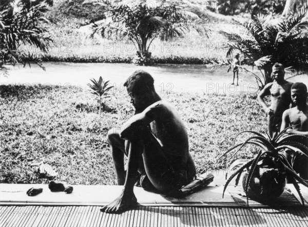 Silent despair. A Congolese man sits on a veranda, contemplating, in silent despair, the severed hand and foot of his five year old daughter, killed along with his wife and son by ABIR militia (Anglo-Belgian India Rubber company). Congo Free State (Democratic Republic of Congo), circa 1904. Congo, Democratic Republic of, Central Africa, Africa.