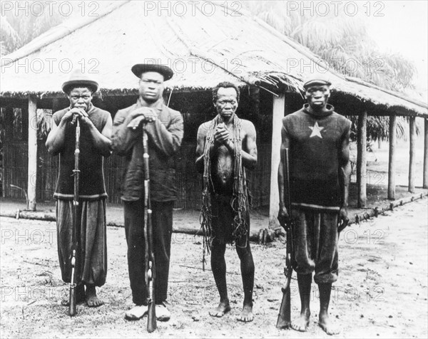 ABIR sentries. Three sentries working for the Anglo-Belgian India Rubber company (ABIR) pose with their guns beside a semi-naked Congolese slave. Congo Free State (Democratic Republic of Congo), circa 1905. Congo, Democratic Republic of, Central Africa, Africa.