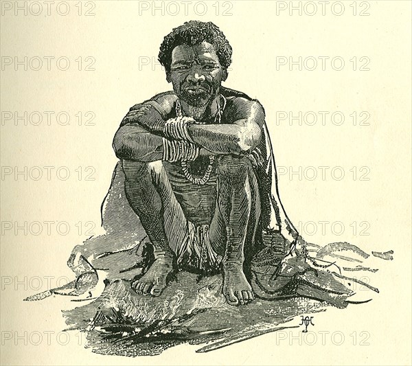 Portrait of a Sudanese slave. Illustration of a Sudanese slave, squatting on the ground beside by a fire. Sudan, circa 1889. Sudan, Eastern Africa, Africa.