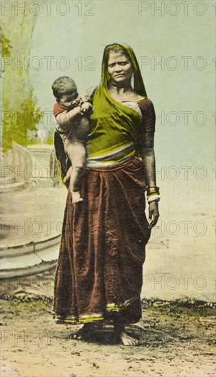Indian woman and child. Portrait of a female Indian labourer, standing barefoot and traditionally dressed in a sari as she balances a baby on her hip. India, circa 1910. India, Southern Asia, Asia.