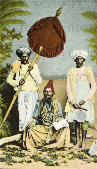 A Hindu priest. A Hindu priest, adorned with beads, is waited on by two men, one of whom shades him with a parasol. India, circa 1910. India, Southern Asia, Asia.