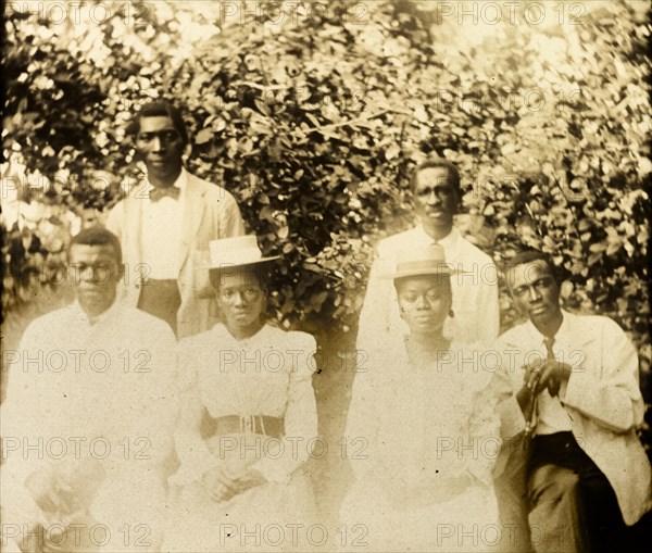 Africans in Western dress. Portrait of a group of African people dressed in Western-style formal attire. The men wear white blazers with ties, the women, long-sleeved white dresses with belted waists and boater hats. Bioko, Equatorial Guinea, circa 1930., Bioko Norte, Equatorial Guinea, Central Africa, Africa.