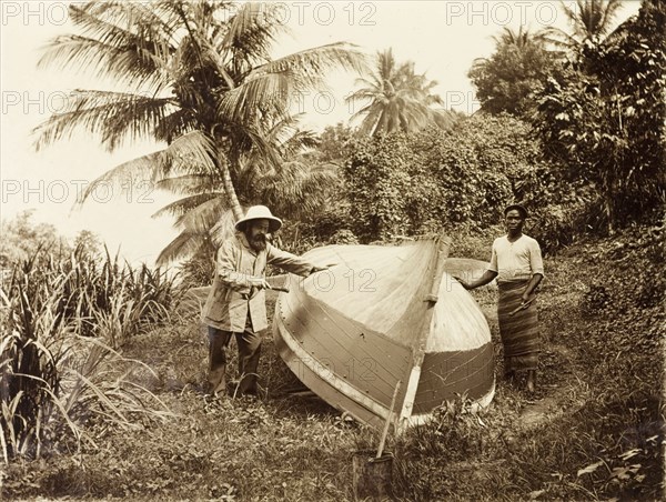Painting the underside. A British Primitive Methodist missionary worker paints the underside of a small boat with the help of an African man. Bioko, Equatorial Guinea, circa 1930., Bioko Norte, Equatorial Guinea, Central Africa, Africa.