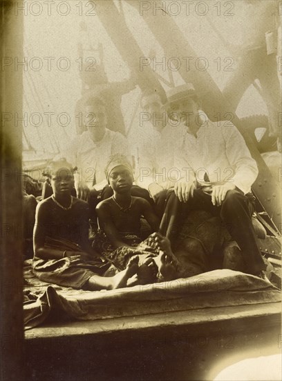 European men, African girls. Three European men accompany two African girls on what appears to be the deck of a ship. This photograph is one of around 70 images compiled by a British Primitive Methodist missionary documenting life on the island of Bioko during the 1930s. Location unknown, circa 1930.