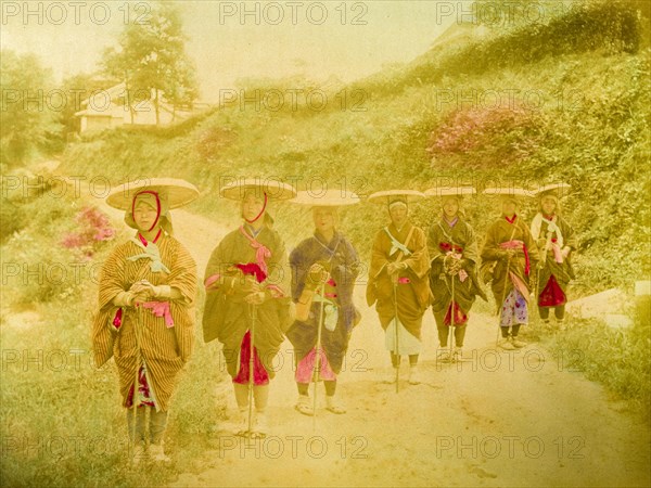 Japanese women. Seven Japanese women stand in line on a rural road. Traditionally dressed in kimonos, they wear flat straw hats secured with chin straps and rags wrapped around their feet. Japan, circa 1910. Japan, Eastern Asia, Asia.