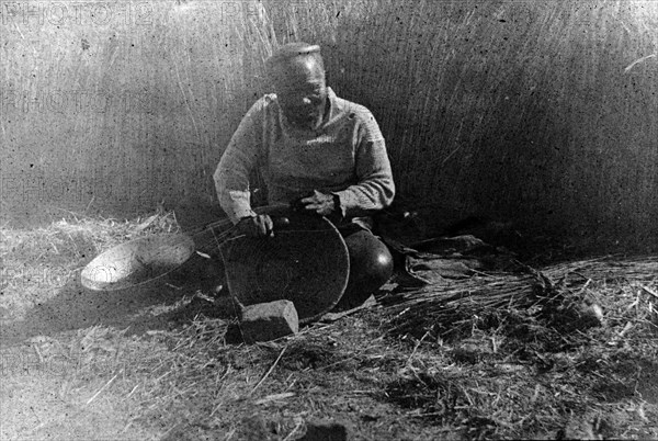 Making a reed bowl, South Africa. An elderly Zulu man sits cross-legged on the ground as he fashions a bowl out of reeds. This photograph was taken during the Second Boer War (1899-1902), a conflict that encroached upon the traditional homelands of the Zulu people. Natal (KwaZulu Natal), South Africa, circa 1901., KwaZulu Natal, South Africa, Southern Africa, Africa.