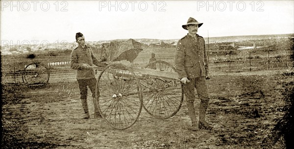 Boer War stretcher-bearers. Two uniformed stretcher-bearers in the British Army carry an empty, wheeled stretcher across a muddy battlefield during the Second Boer War (1899-1902). The man on the left appears to be Indian, and may have been one of thousands of Indian Army officers shipped to South Africa to help the British fight the Boers. South Africa, circa 1900. South Africa, Southern Africa, Africa.
