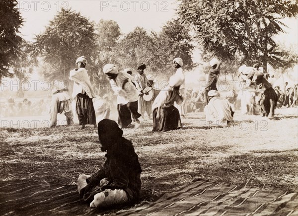 Indian drummers. A drummer is encircled by male dancers in traditional Indian dress during an outdoor musical performance. Onlookers gather around the circle to watch the dance. India, circa 1930. India, Southern Asia, Asia.