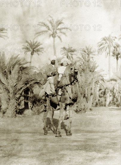 Margarert Lawrence rides a camel. Margaret Lawrence (b.1904), the daughter of Phyllis and Sir Henry Staveley Lawrence (Collector of Karachi), sits on a saddled camel in front of an Indian servant who holds the reins. Karachi, India (Pakistan), circa 1910. Karachi, Sindh, Pakistan, Southern Asia, Asia.