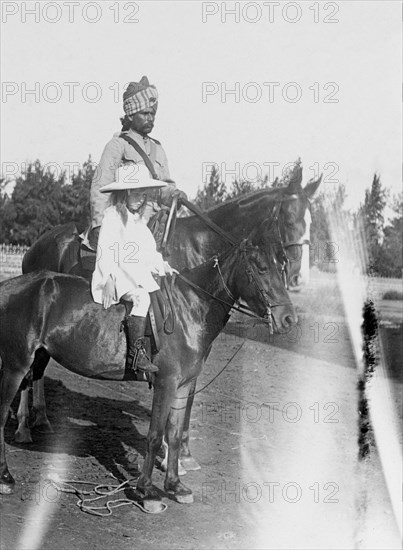 Margaret Lawrence rides with a 'sowar'. Margaret Lawrence (b.1904), the daughter of Phyllis and Sir Henry Staveley Lawrence (Collector of Karachi), sits on a pony beside a turbaned 'sowar' (cavalry soldier) of the Indian Army who rides a horse. Karachi, India (Pakistan), circa 1912. Karachi, Sindh, Pakistan, Southern Asia, Asia.