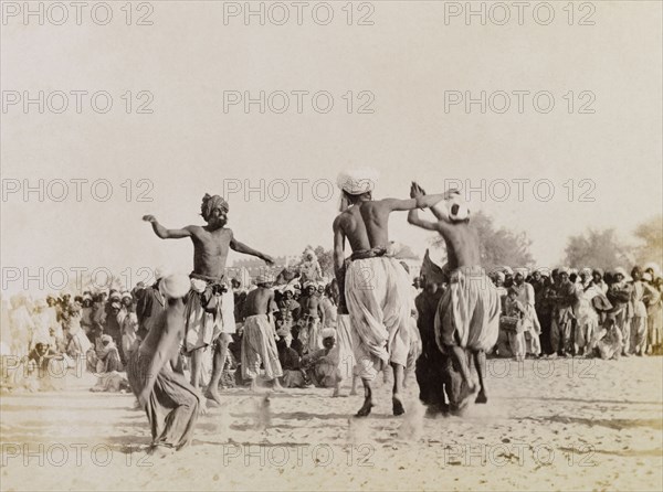 Male Indian dancers. Four male dancers leap into the air as they perform in front of a large crowd of spectators. Sukkur, Sind, India (Sindh, Pakistan), circa 1908. Sukkur, Sindh, Pakistan, Southern Asia, Asia.