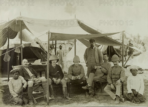 Civil Officers at Wuntho. Six British Civil Officers pose for the camera beneath the awning of a tent, attended by their Burmese servants. The group supported the British Army in a campaign to suppress Burmese rebels in Wuntho State (today known as the Sagaing Division). Wuntho, Burma (Myanmar), 1891. Wuntho, Sagaing, Burma (Myanmar), South East Asia, Asia.