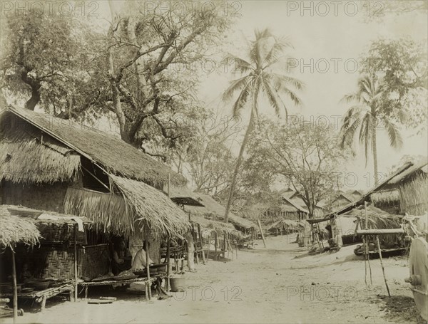 An empty road in Wuntho. Two street-sellers sit in the shade of a thatched awning, waiting to offer their wares to passers-by at the side of an empty road. This scene was captured shortly after British forces took control of Wuntho following a conflict with Burmese rebels. Wuntho, Burma (Myanmar), 1891. Wuntho, Sagaing, Burma (Myanmar), South East Asia, Asia.