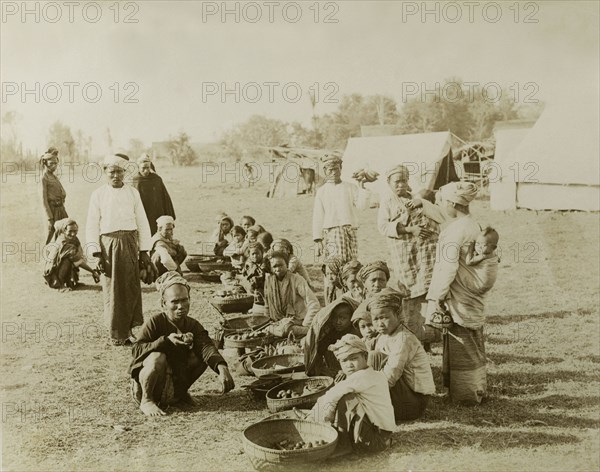An outdoor bazaar at Wuntho. A line of women and children sell food from baskets on the ground outside a British Army military camp. The tents in the background were erected during a campaign to suppress Burmese rebels in Wuntho State (today known as the Sagaing Division). Sagaing, Burma (Myanmar), 1891., Sagaing, Burma (Myanmar), South East Asia, Asia.