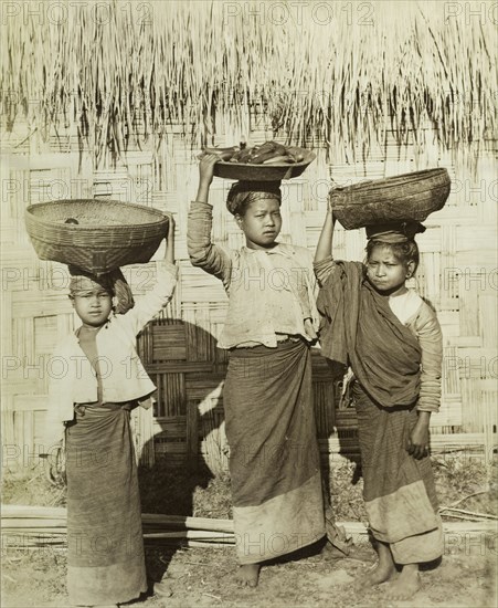 Three Burmese girls at Wuntho. Three young Burmese girls pose outside a thatched dwelling, balancing baskets of ripe bananas on their heads. Wuntho, Burma (Myanmar), circa 1891. Wuntho, Sagaing, Burma (Myanmar), South East Asia, Asia.