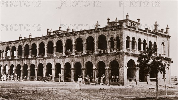 Government House at Wad Madani. View of Government House at Wad Madani, a long, two-storey building with an open arcade running the length of its facade and pinnicles projecting from its parapet. Wad Madani, Sudan, circa 1910. Wad Madani, Al Jazirah, Sudan, Eastern Africa, Africa.