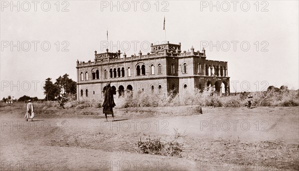 Government House at Wad Madani. View of Government House at Wad Madani, a large, two-storey building with rounded arch windows, pinnicles along its parapet, and two square towers. Wad Madani, Sudan, circa 1910. Wad Madani, Al Jazirah, Sudan, Eastern Africa, Africa.