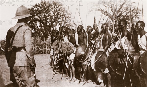 Sudanese warriors receive a 'Sirdar'. A British 'Sirdar' (Commander-in-Chief) of the Anglo-Egyptian army visits a group of Sudanese warriors. He stands with his back to the camera, facing the men, who wear traditional dress and carry long spears and shields. Er Rosieres, Sudan, circa 1910. Er Roseires, Blue Nile, Sudan, Eastern Africa, Africa.