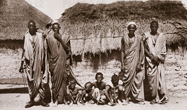 Bataheen men and children, Sudan. Four Sudanese men pose for the camera with four small children outside a mud-walled dwelling. An original caption identifies them as 'Battaheen (Bataheen) Arabs', one of several distinct tribal groups resident in the northern states of Sudan. Probably Al Qadarif State, Sudan, circa 1910., Al Qadarif, Sudan, Eastern Africa, Africa.