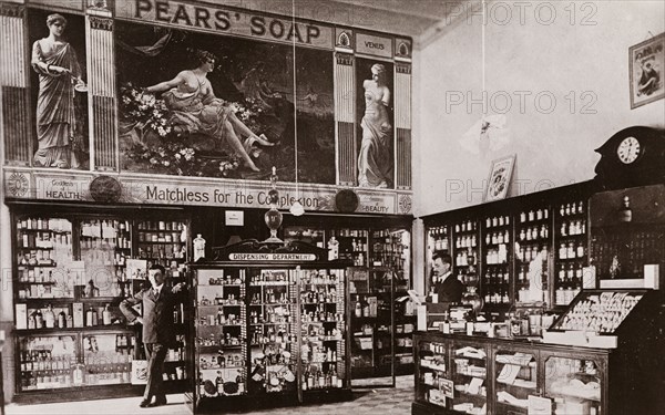 Inside the English Pharmacy, Khartoum. Interior view of the English Pharmacy in Khartoum. Glass-fronted cases packed with bottles line the walls beneath a huge advertisement for 'Pear's Soap'. A European man in a suit leans against a free-standing dispensing cabinet, whilst a cashier consults a piece of paper at the counter. Khartoum, Sudan, circa 1910. Khartoum, Khartoum, Sudan, Eastern Africa, Africa.