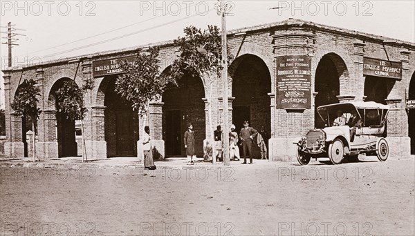Outside the English Pharmacy, Khartoum. Exterior view of the English Pharmacy in Khartoum, an arcaded, brick building with a flat roof. Banners hanging from the building read 'The English Pharmacy' and 'The English Drugstore', along with an advertisement for 'Burroughs Wellcome & Co.' products. Khartoum, Sudan, circa 1910. Khartoum, Khartoum, Sudan, Eastern Africa, Africa.